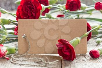 Blank tag with carnations on wooden background. Copy-space.