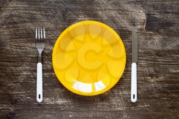   Empty yellow plate, fork and knife on wooden background. Top view with text space