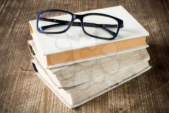 Books and reading glasses on the wooden background.