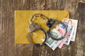 Envelope with Euro bills and handcuffs over wooden background