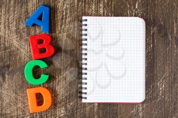 ABCD spelling from plastic letters and blank notebook on wooden background