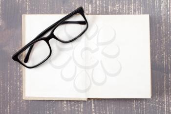 Open book and reading glasses on the wooden background.Top view.