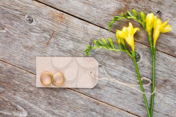  Yellow freesia flowers with blank tag and wedding rings on old wooden background
