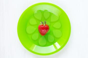 Fresh single strawberry in green plate on the white wooden table
