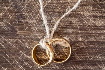  Wedding rings hanging on rope over wooden background.