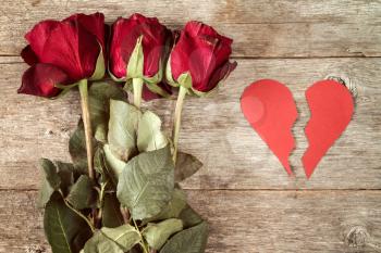 Divorce concept - red broken heart with dry roses on wooden background
