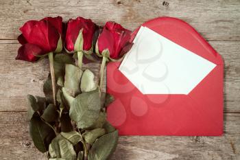 Red envelope with blank mail and old roses on wooden background