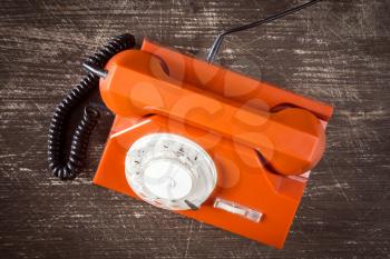 Old orange retro phone with rotary dial. Top view on wooden background.