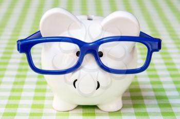 Piggy bank with blue glasses on checkered tablecloth 