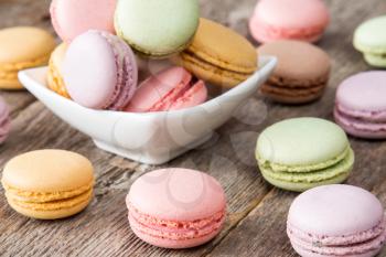French colorful and tasty macarons in a bowl on wooden background