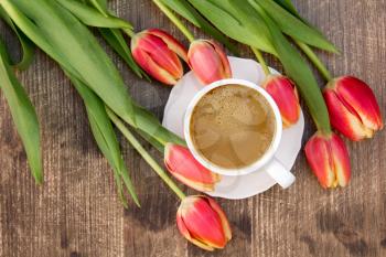 Bunch of red tulips and white cup of coffee on the brown wooden table