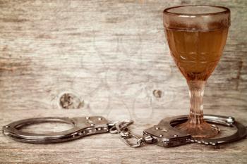 Glass of alcohol with handcuffs as symbol for alcohol abuse
