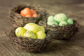 Three nests with painted eggs on wooden background. 