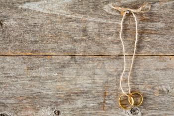Two gold wedding rings tied with string hanging on wooden wall