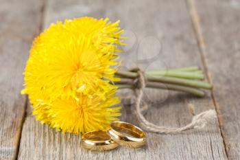 Wedding rings and bunch of yellow dandelion flowers on wooden background