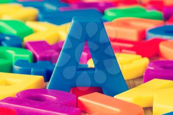 Blue letter A in a pile of other colorful plastic letters.