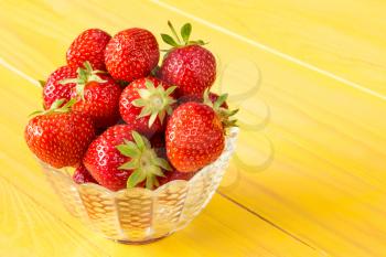 Glass bowl full of red strawberries on yellow wooden background