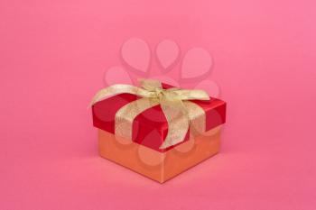 Gift box with golden bow on the pink background