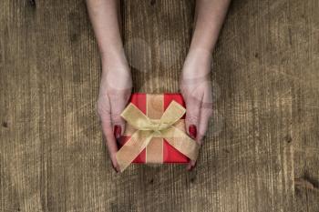 Flat lay of woman hands holding gift decorated with bow 