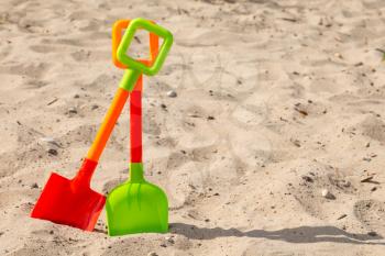 Two colorful plastic shovels on the beach sand