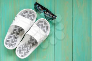 Summer holiday background. White flip flops and sunglasses on blue wooden background.