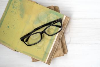 Black eyeglasses on books placed on white wooden background. Top view, copy space.