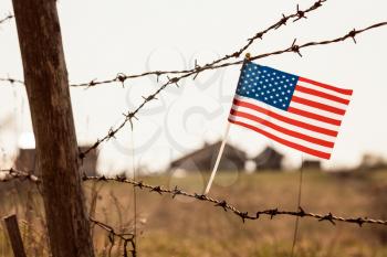 American flag on old barbed wire fence. Blurred buildings in the background.