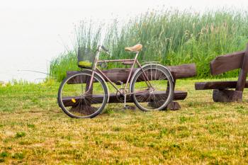 Old bicycle leaning against wooden bench on the lake side