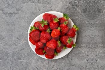 Red strawberry in a plate on grey stone background