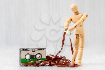 Wooden man pulling out the tape from an old audio cassette , vintage outdated technology concept