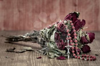 Bouquet of faded roses with catholic rosary. Faith and hope concept.