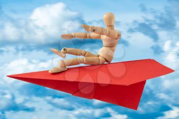 Wooden doll with paper plane flying on blue sky with clouds. Travel or tourism concept.