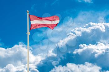 Latvian national flag waving on wind against blue cloudy sky