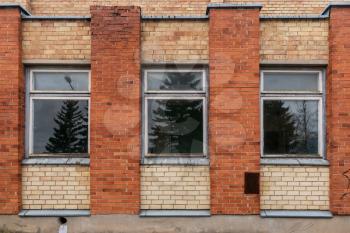 Three windows of an abandoned house. An outside windows wall with damaged red bricks. 