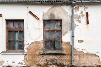 Two windows in damaged wall of an abandoned house. An outside window wall with paint peeling and damaged. 
