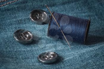 Needle, buttons and spool of thread on jeans fabric