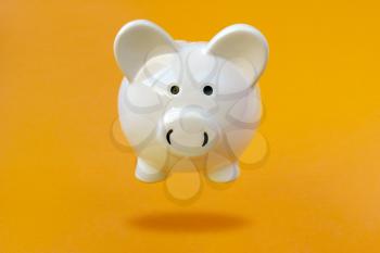 White Piggy bank levitating over a yellow background. Financial concept.