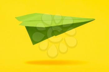 Green paper aircraft fly over yellow background