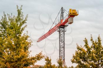 Construction tower crane against the sky. High-altitude slewing crane on a background of rainy sky and tree crowns
