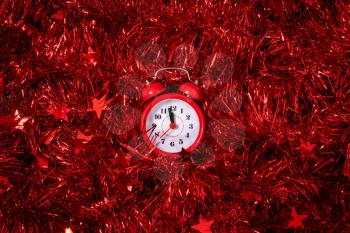 Counting last minutes before Christmas or New Year. Countdown to midnight. Red alarm clock lying on table in bright garland and tinsel close up.
