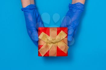 Hands in protective gloves gives gift box. Pandemic winter holidays celebration. Quarantine hygiene. 