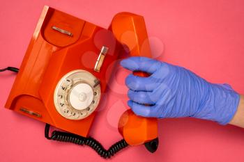 Hand in blue medical glove holding old telephone receiver. Conceptual image.