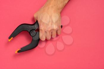 Hand holding large plastic spring clamp on pink background. Copy space.