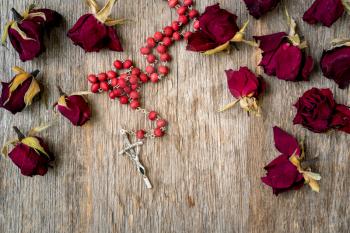 Faith and spirituality concept. Rosary and dry rose buds on the wooden background