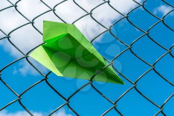 Green paper plane gets stuck in metal fence