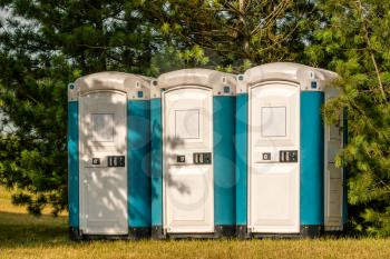 Three plastic portable toilets at an outdoor event