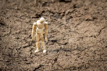 Wooden man standing on soil dry land, looking sad and frustrated thinking about problems