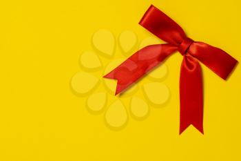 Red ribbon satin gift bow on the yellow background. Copy space.