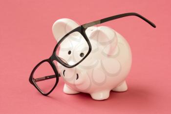 Piggy bank and eyeglasses on the pink background. Financial concept.
