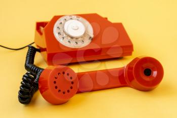 Retro orange telephone on yellow background, focus is on the handset
